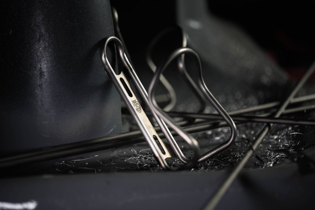 Silca Sicuro Titanium Bottle Cage Silca Sicuro Titanium Bottle Cage leaning a agaisnt a grey back drop